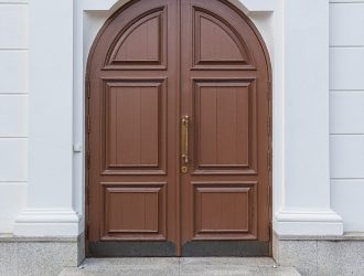 Brown wooden arched door with lamp above it and granite tile steps